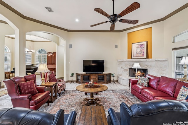 living area with ceiling fan with notable chandelier, a premium fireplace, baseboards, tile patterned floors, and crown molding