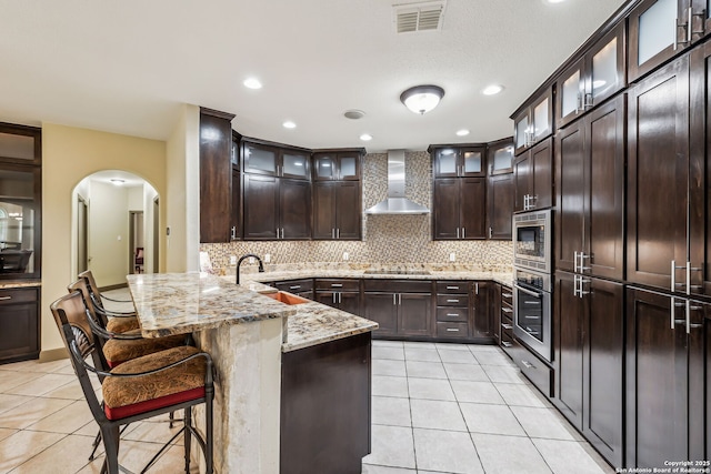 kitchen featuring light tile patterned floors, visible vents, wall chimney exhaust hood, appliances with stainless steel finishes, and a peninsula