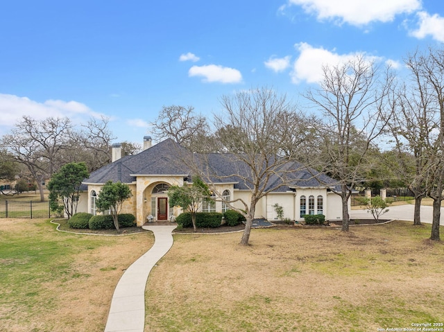 french country home featuring a chimney, fence, a front lawn, and stucco siding