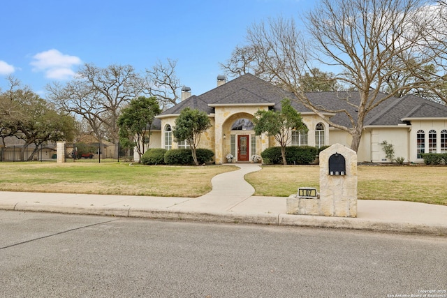 french country home featuring a front lawn, a chimney, and fence