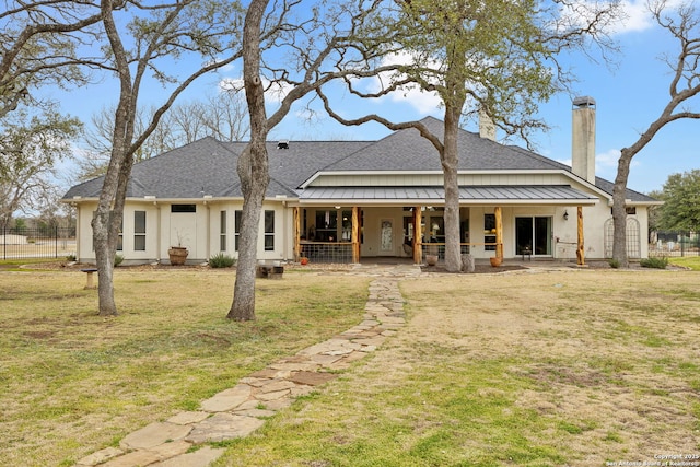 back of property with metal roof, roof with shingles, a standing seam roof, a yard, and stucco siding