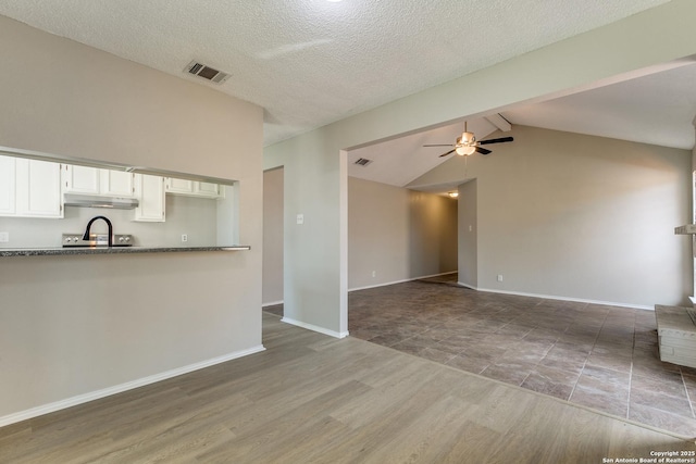 unfurnished living room with vaulted ceiling with beams, wood finished floors, visible vents, baseboards, and a ceiling fan