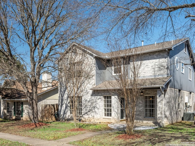 traditional-style home with brick siding, roof with shingles, and central AC unit