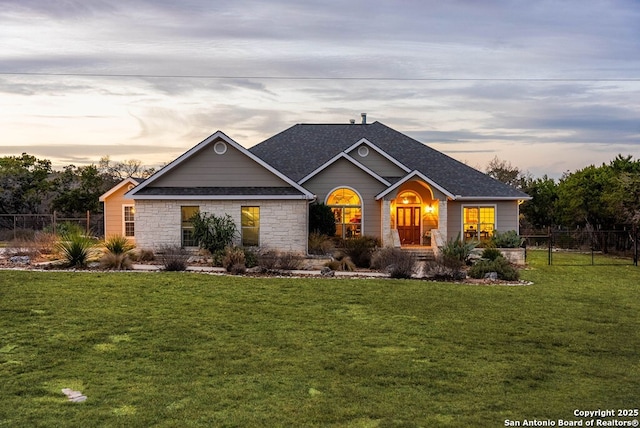 craftsman inspired home featuring stone siding, roof with shingles, fence, and a front yard