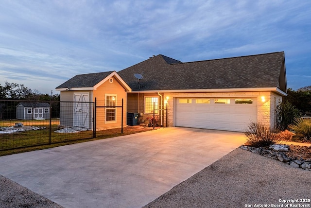 view of front of home with a garage, a shingled roof, central AC unit, concrete driveway, and a shed