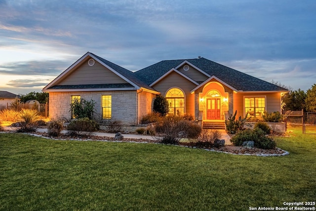 ranch-style home with stone siding, a front lawn, roof with shingles, and fence