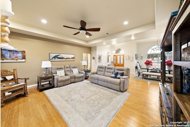 living room featuring light wood finished floors, visible vents, baseboards, a tray ceiling, and recessed lighting