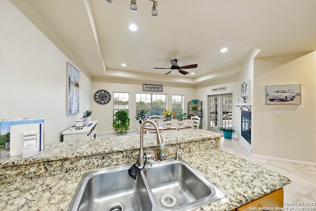 kitchen featuring light stone counters, recessed lighting, a raised ceiling, and a sink