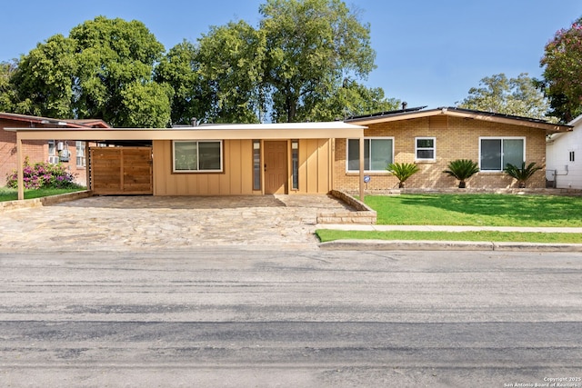 single story home with driveway, an attached carport, a front yard, board and batten siding, and brick siding