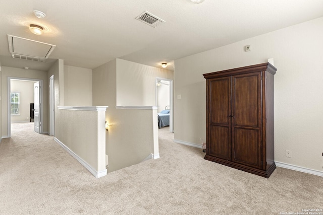 hall featuring attic access, light colored carpet, visible vents, and an upstairs landing