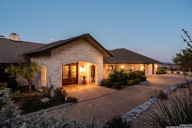 view of front of home with driveway, stone siding, a shingled roof, and an attached garage