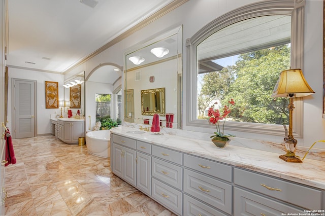 bathroom with a tub to relax in, marble finish floor, crown molding, two vanities, and visible vents