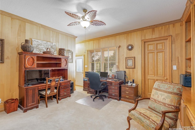 carpeted home office with ornamental molding, a textured ceiling, wooden walls, and a ceiling fan