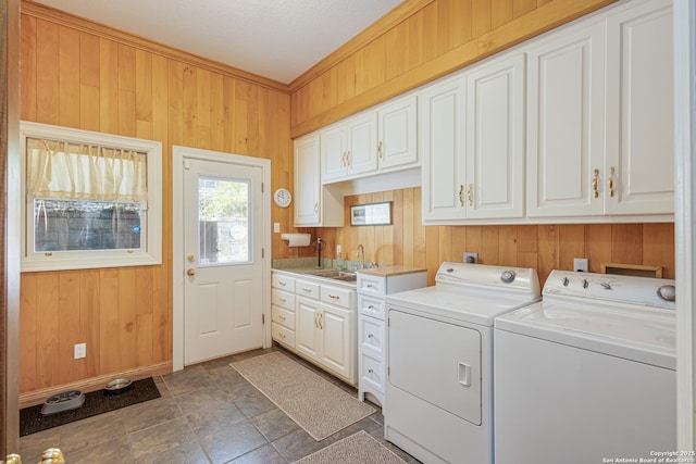 washroom featuring cabinet space, a sink, wooden walls, and washing machine and clothes dryer