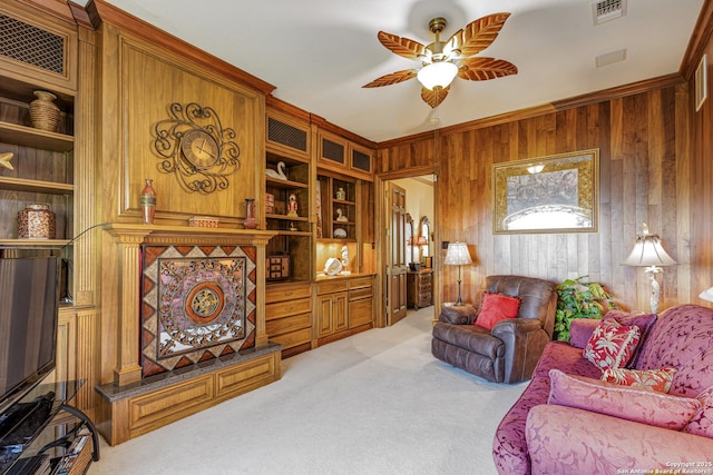 living room with crown molding, light colored carpet, visible vents, a ceiling fan, and wooden walls