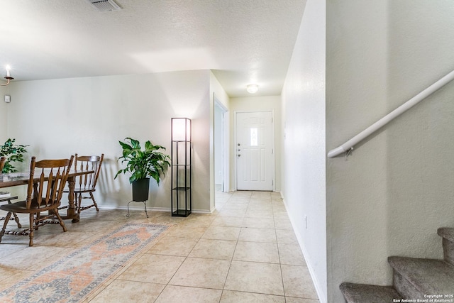 entryway with light tile patterned floors, visible vents, baseboards, stairway, and a textured ceiling