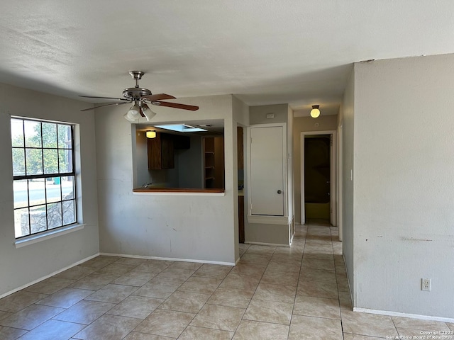 empty room with light tile patterned floors, a textured ceiling, baseboards, and a ceiling fan