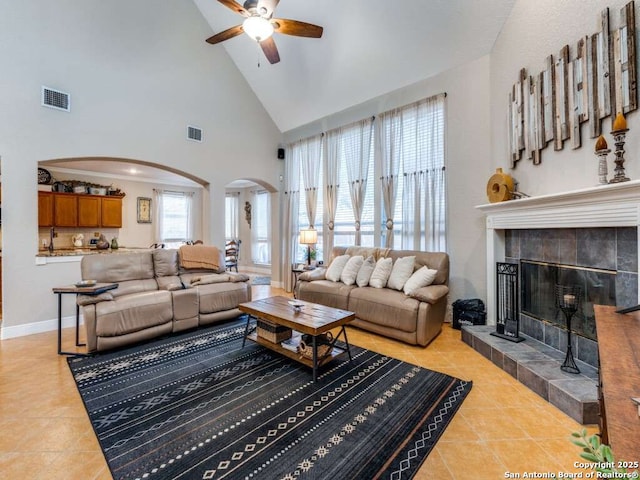 living room with arched walkways, light tile patterned flooring, a tile fireplace, and visible vents