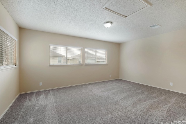 carpeted empty room featuring a textured ceiling, attic access, and baseboards