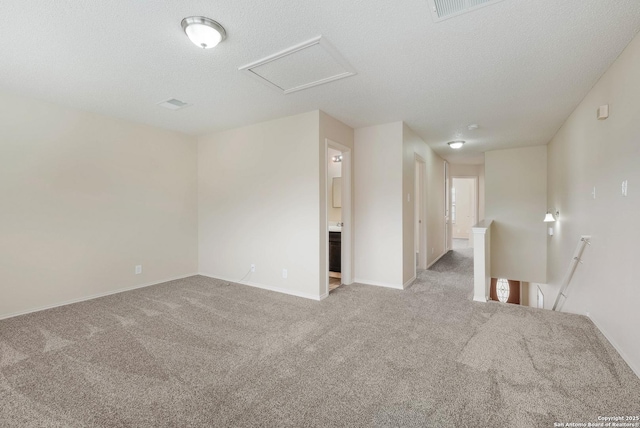 spare room with attic access, carpet, visible vents, and a textured ceiling