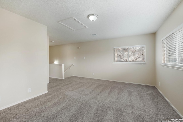 carpeted spare room with attic access, baseboards, and a textured ceiling