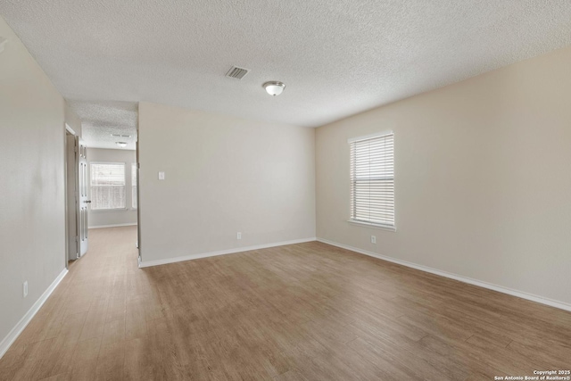 unfurnished room with baseboards, a textured ceiling, visible vents, and wood finished floors