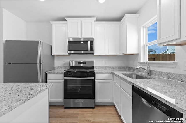 kitchen featuring stainless steel appliances, light wood-style flooring, white cabinets, a sink, and light stone countertops