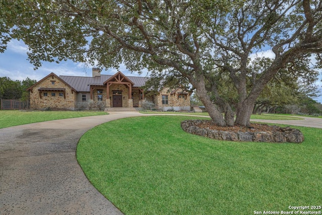 view of front of house with metal roof, driveway, stone siding, a standing seam roof, and a front yard