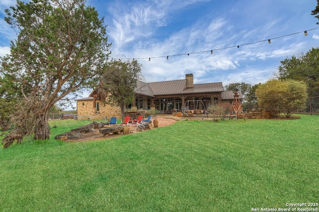 rear view of property with a patio, a chimney, metal roof, a standing seam roof, and a yard