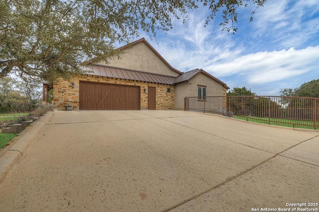 view of front of house featuring driveway, a garage, a standing seam roof, fence, and stucco siding