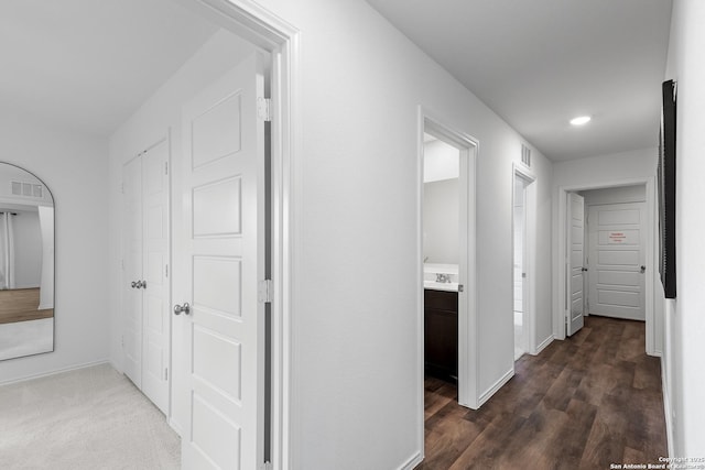 hall with dark wood-type flooring, visible vents, and baseboards