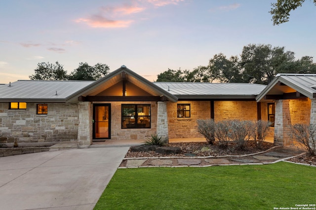 view of front of property with metal roof, a porch, stone siding, a standing seam roof, and a front yard