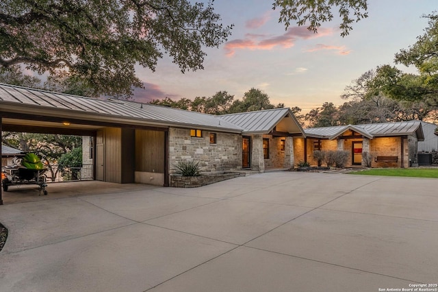 view of front of house with a standing seam roof, metal roof, an attached carport, stone siding, and driveway