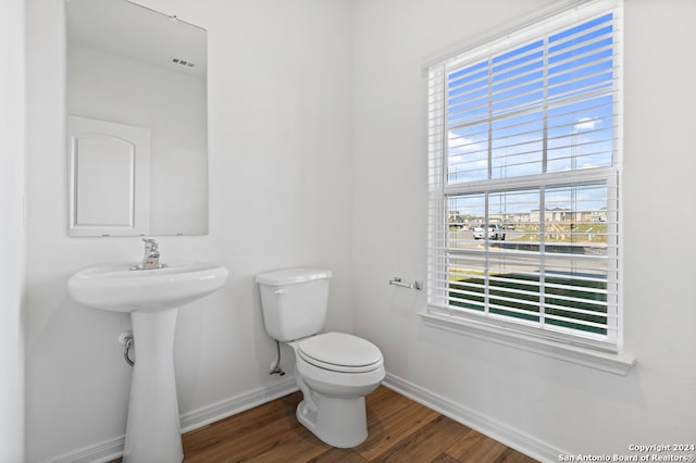 half bathroom with a wealth of natural light, toilet, baseboards, and wood finished floors