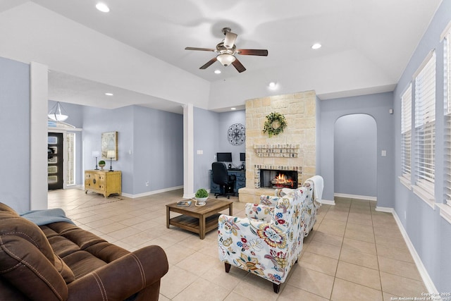 living area featuring light tile patterned floors, baseboards, vaulted ceiling, and a stone fireplace