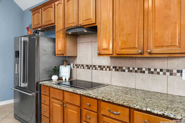 kitchen with light stone countertops, under cabinet range hood, black electric stovetop, and decorative backsplash