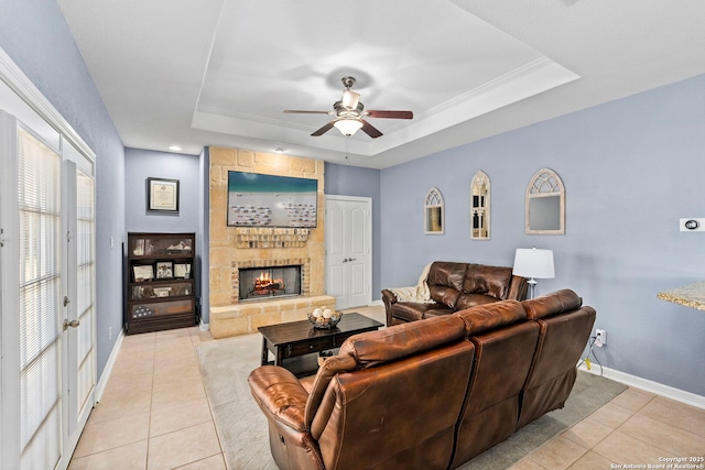 living room featuring a tray ceiling, a fireplace, light tile patterned flooring, ceiling fan, and baseboards