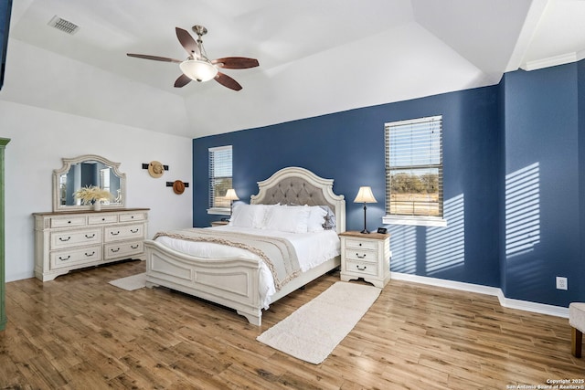 bedroom with lofted ceiling, multiple windows, wood finished floors, and visible vents