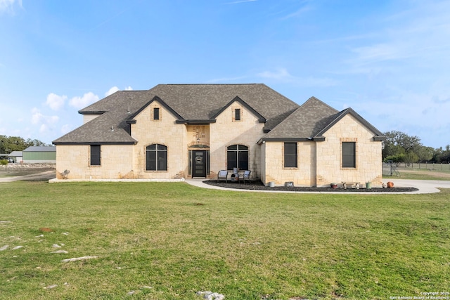 french country inspired facade with a front lawn and roof with shingles