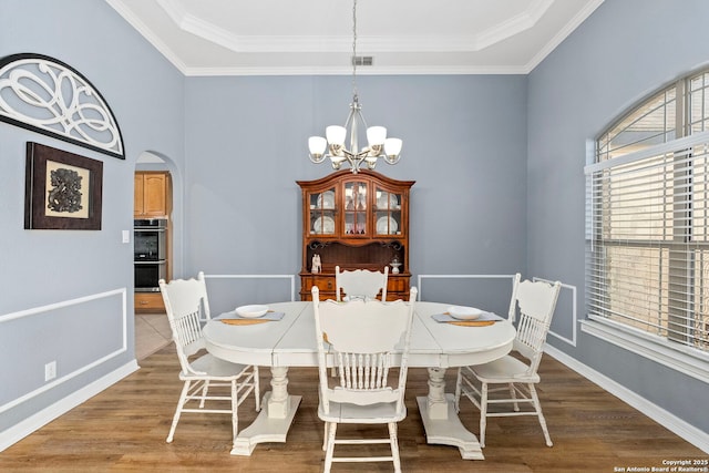 dining space featuring arched walkways, a chandelier, wood finished floors, and ornamental molding