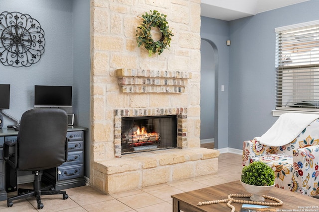 tiled office featuring arched walkways, a stone fireplace, and baseboards