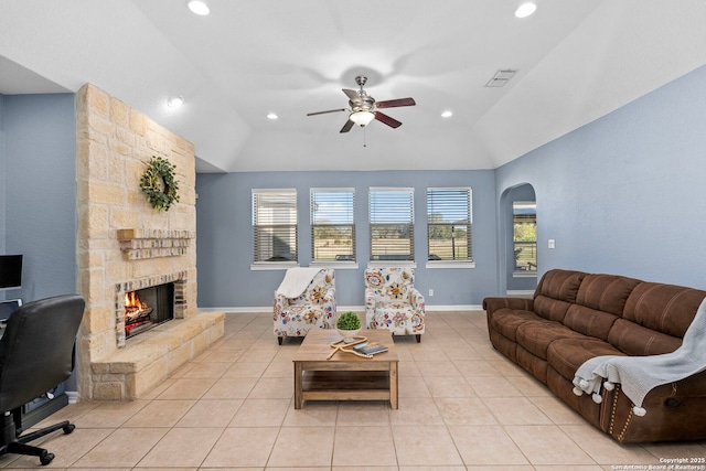 living room with arched walkways, light tile patterned flooring, vaulted ceiling, and a stone fireplace