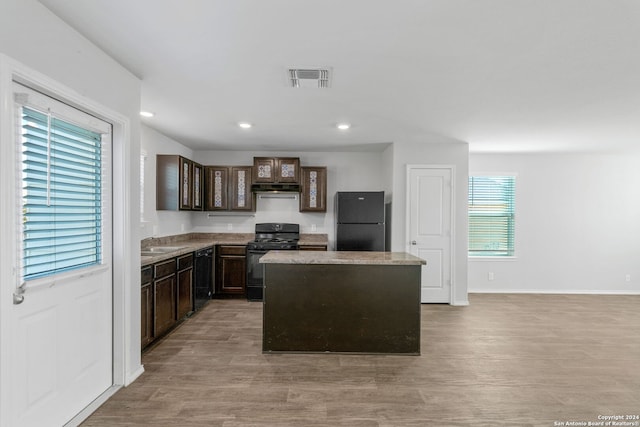 kitchen featuring a center island, visible vents, light wood-type flooring, under cabinet range hood, and black appliances