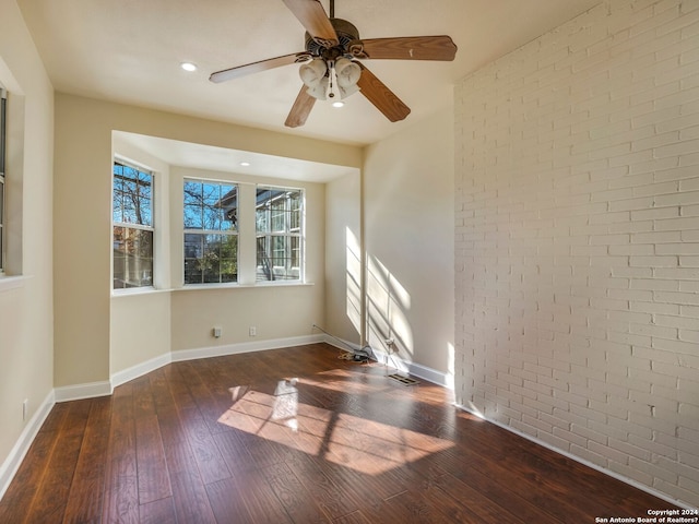 empty room with brick wall, wood-type flooring, baseboards, and ceiling fan