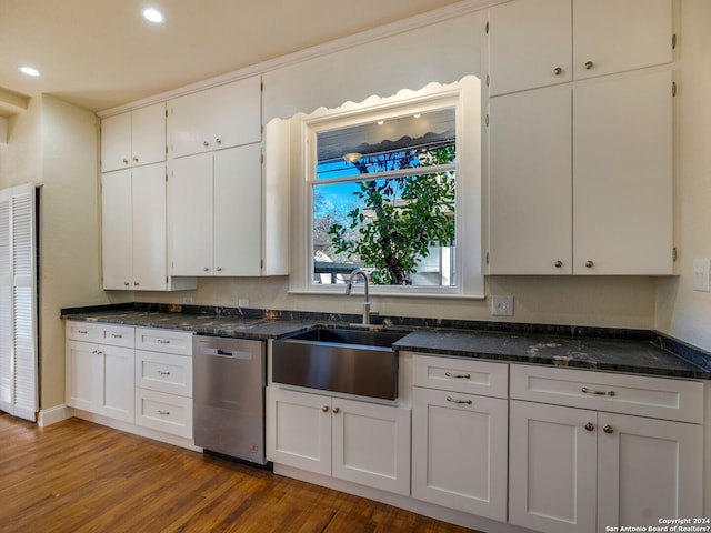 kitchen with dark stone counters, white cabinets, wood finished floors, stainless steel dishwasher, and a sink