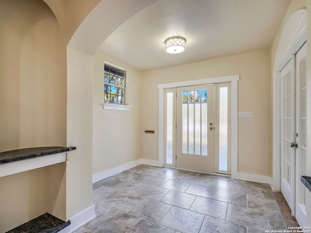 foyer entrance featuring a healthy amount of sunlight, stone tile floors, baseboards, and arched walkways