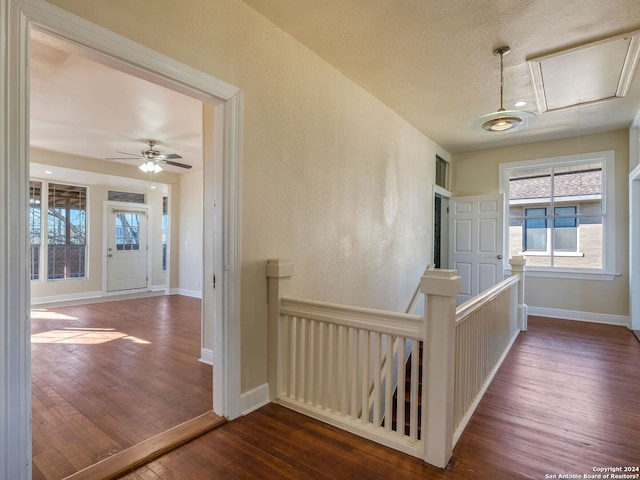 corridor featuring dark wood-style floors, attic access, baseboards, and an upstairs landing