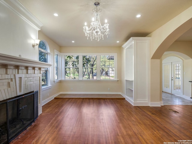 unfurnished living room featuring arched walkways, visible vents, baseboards, and hardwood / wood-style flooring