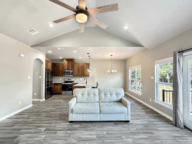 living room with arched walkways, wood finished floors, visible vents, baseboards, and vaulted ceiling