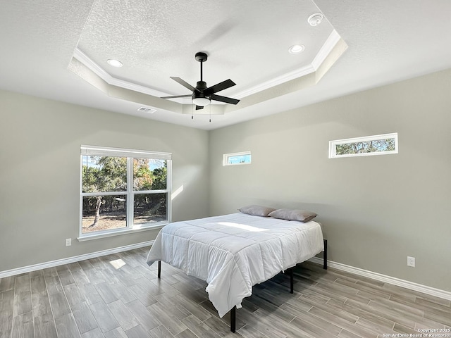 bedroom featuring a tray ceiling, visible vents, baseboards, and wood finish floors